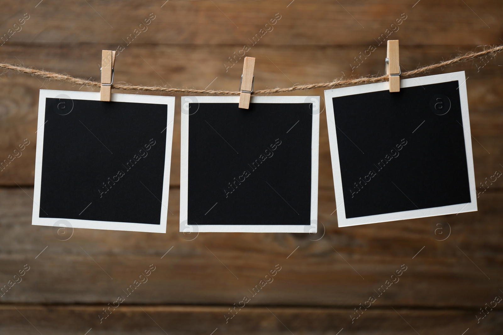 Photo of Clothespins with empty instant frames on twine against wooden background. Space for text