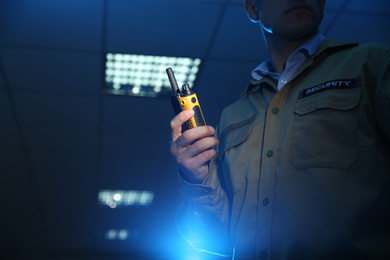 Professional security guard with portable radio set in dark room, closeup