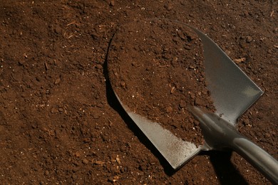 Photo of Metal shovel on fertile soil, top view and space for text. Gardening tool