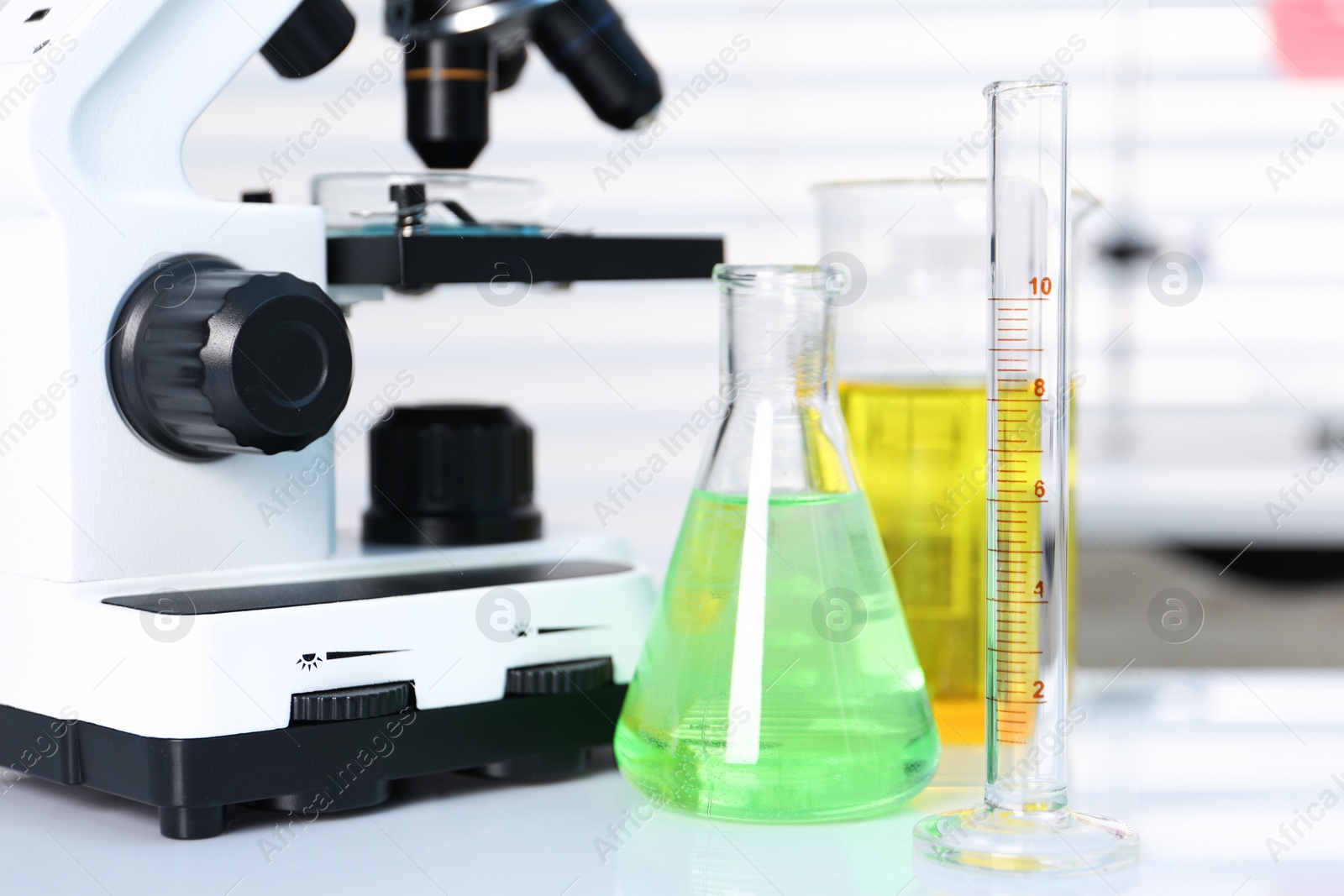 Photo of Laboratory analysis. Different glassware with liquids and microscope on white table indoors