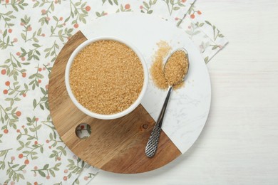 Photo of Brown sugar in bowl and spoon on white wooden table, top view