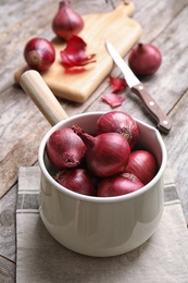 Saucepan with ripe red onions on wooden table