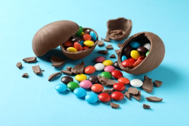 Photo of Broken chocolate eggs with candies on light blue background