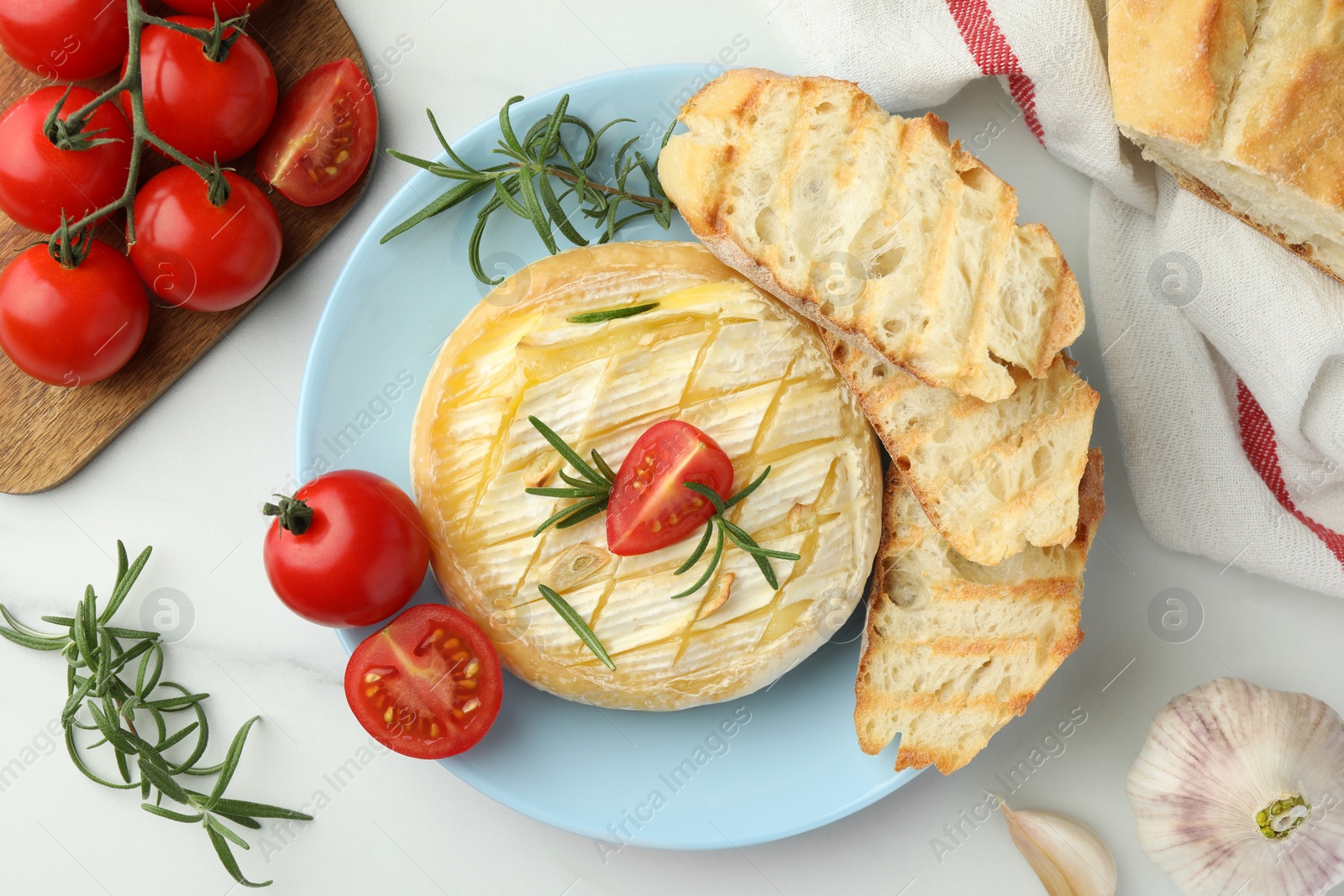 Photo of Tasty baked brie cheese served on white marble table, flat lay