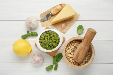 Delicious pesto sauce in bowl and ingredients on white wooden table, flat lay