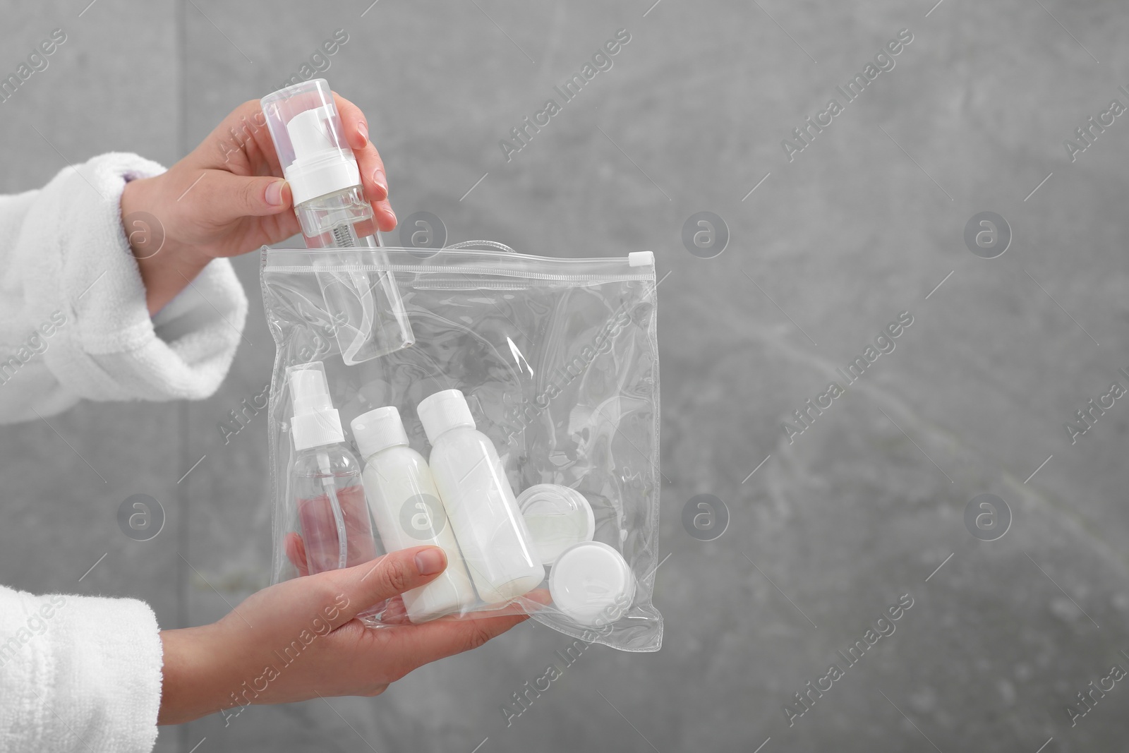 Photo of Woman packing cosmetic travel kit near grey wall closeup and space for text. Bath accessories