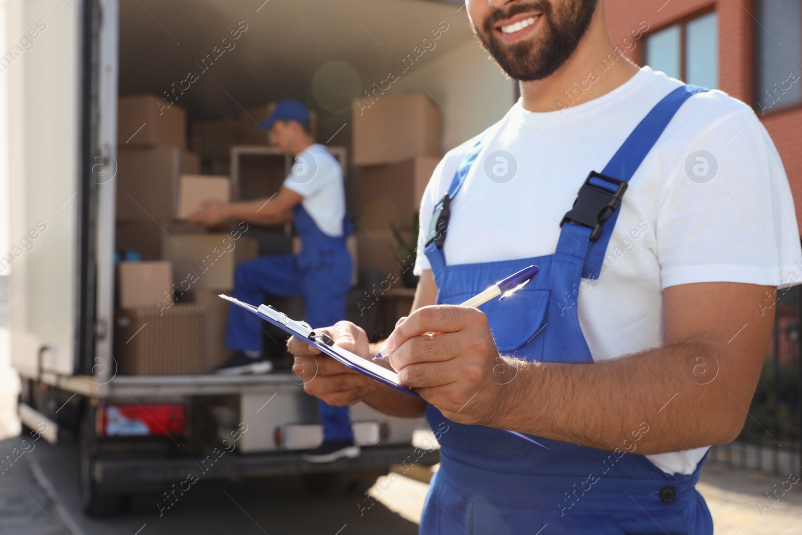 Photo of Moving service workers outdoors, unloading boxes and checking list