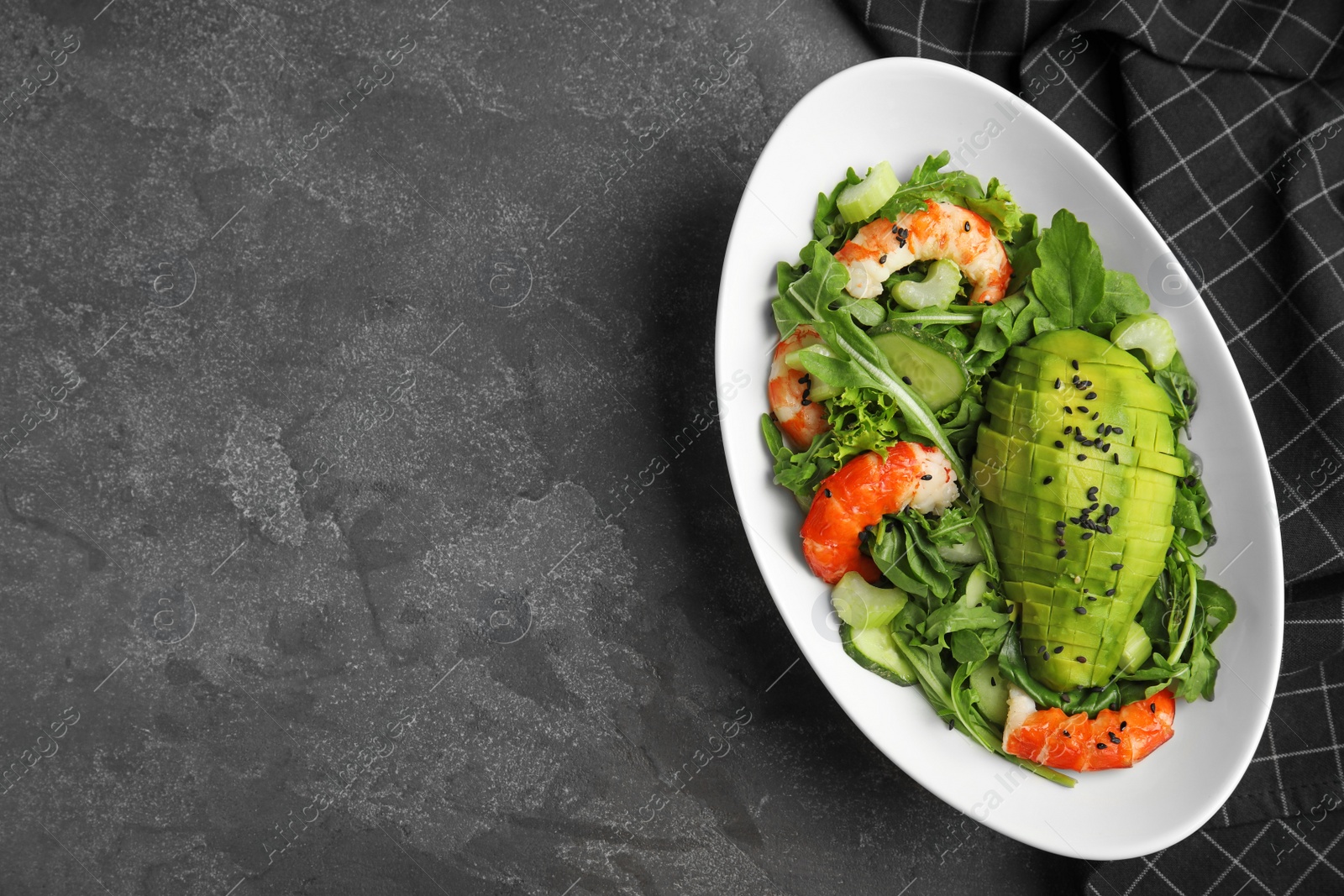 Photo of Delicious avocado salad with shrimps in bowl on grey table, flat lay. Space for text