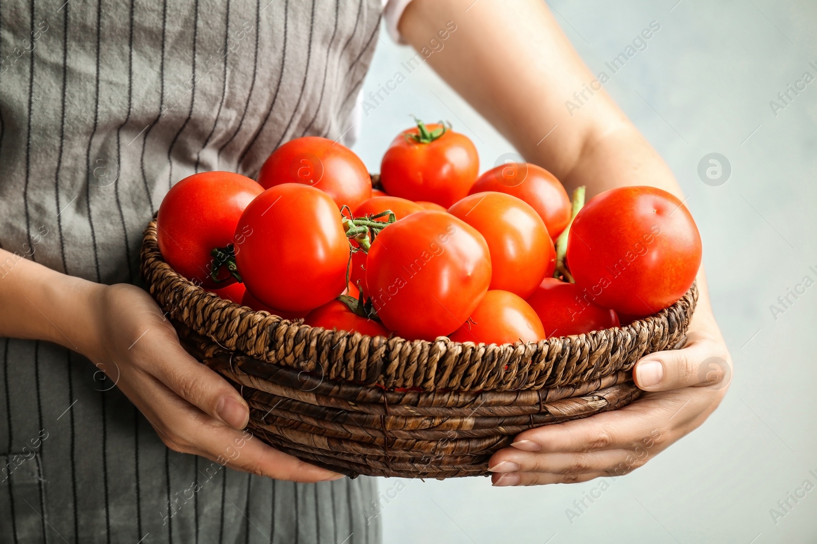 Photo of Woman holding wicker bowl with ripe tomatoes, closeup