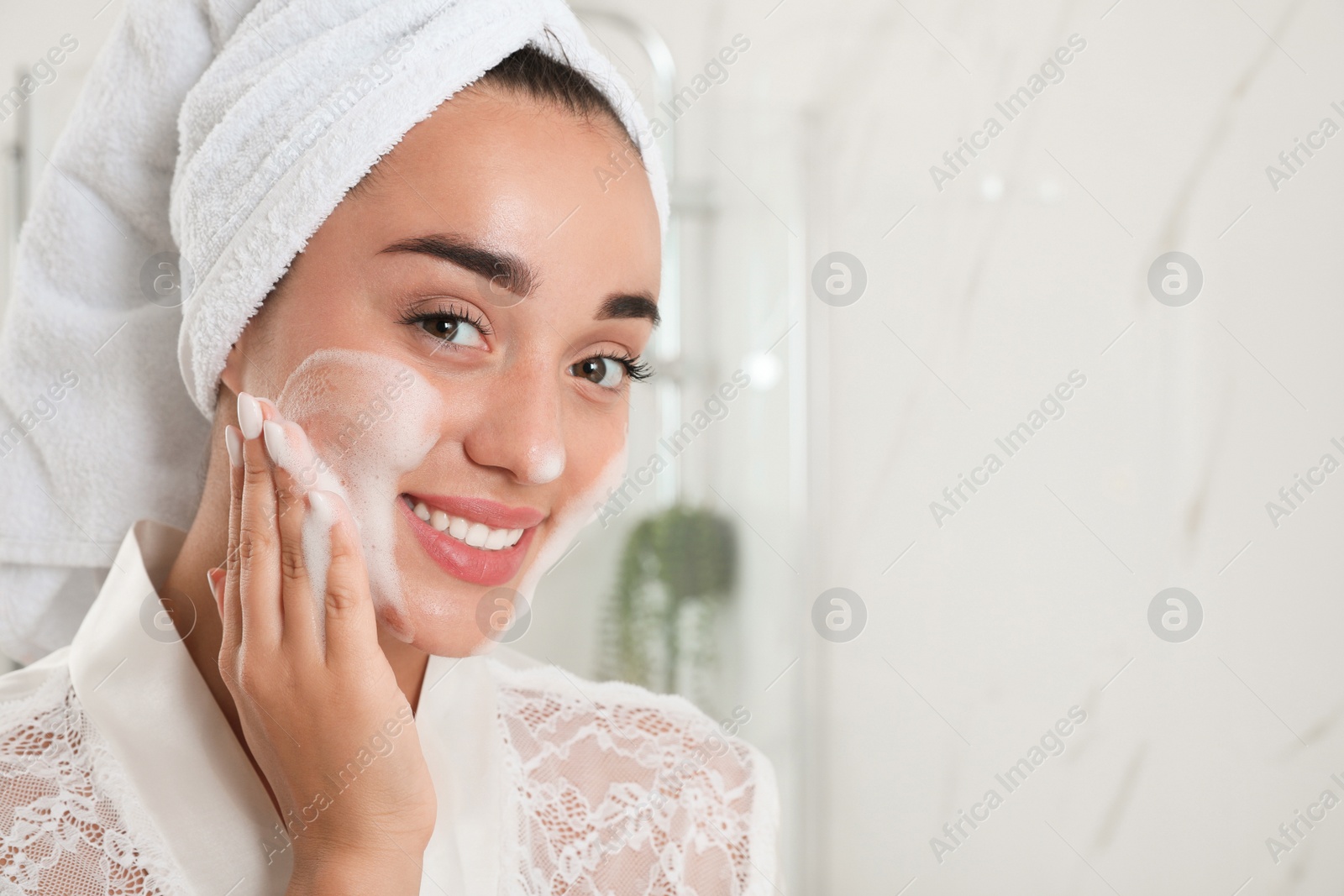 Photo of Beautiful young woman applying cleansing foam onto face in bathroom, space for text. Skin care cosmetic