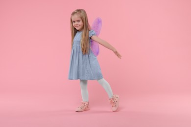 Photo of Cute little girl in fairy costume with violet wings on pink background