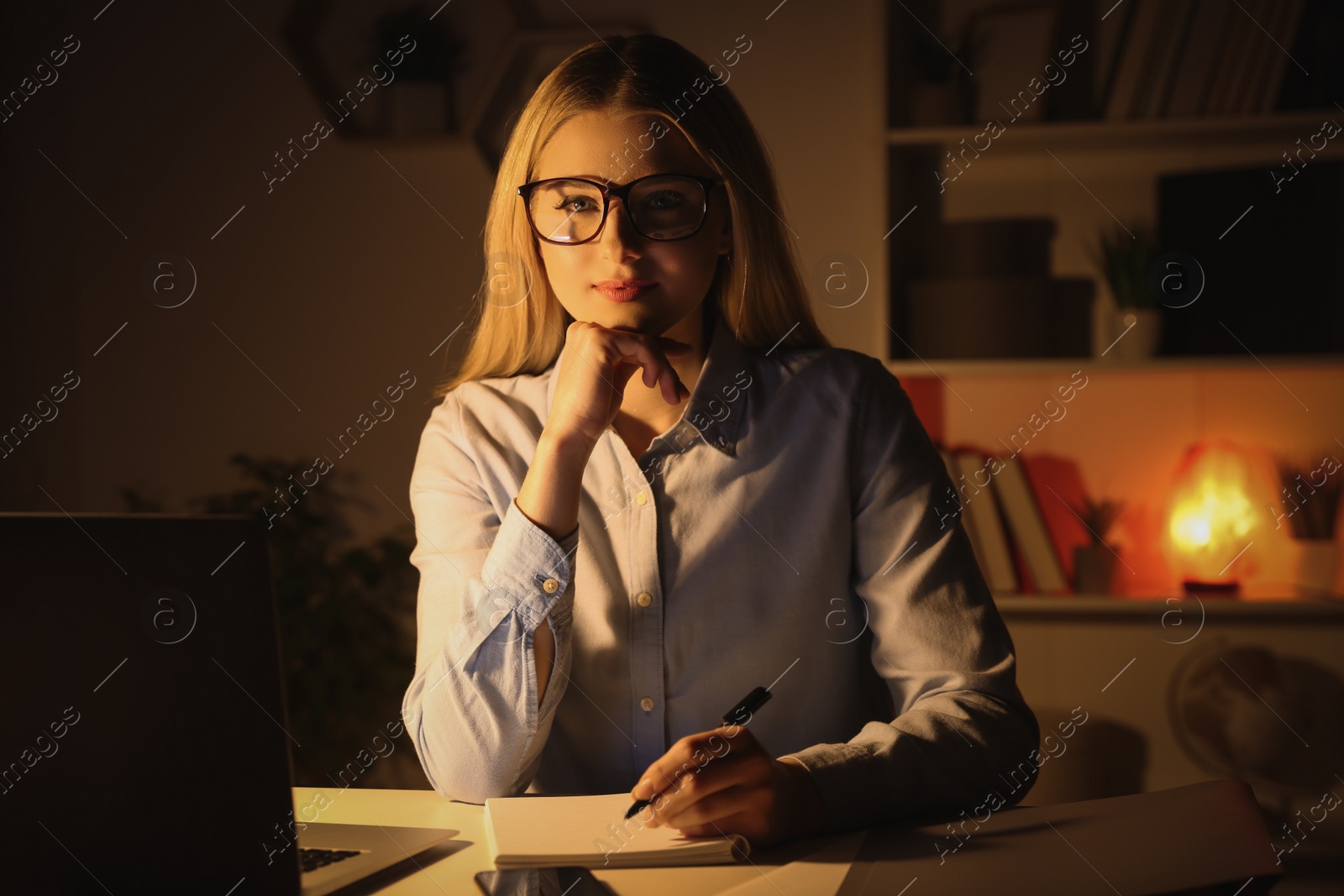 Photo of Home workplace. Portrait of woman with pen and notebook near laptop at white desk in room