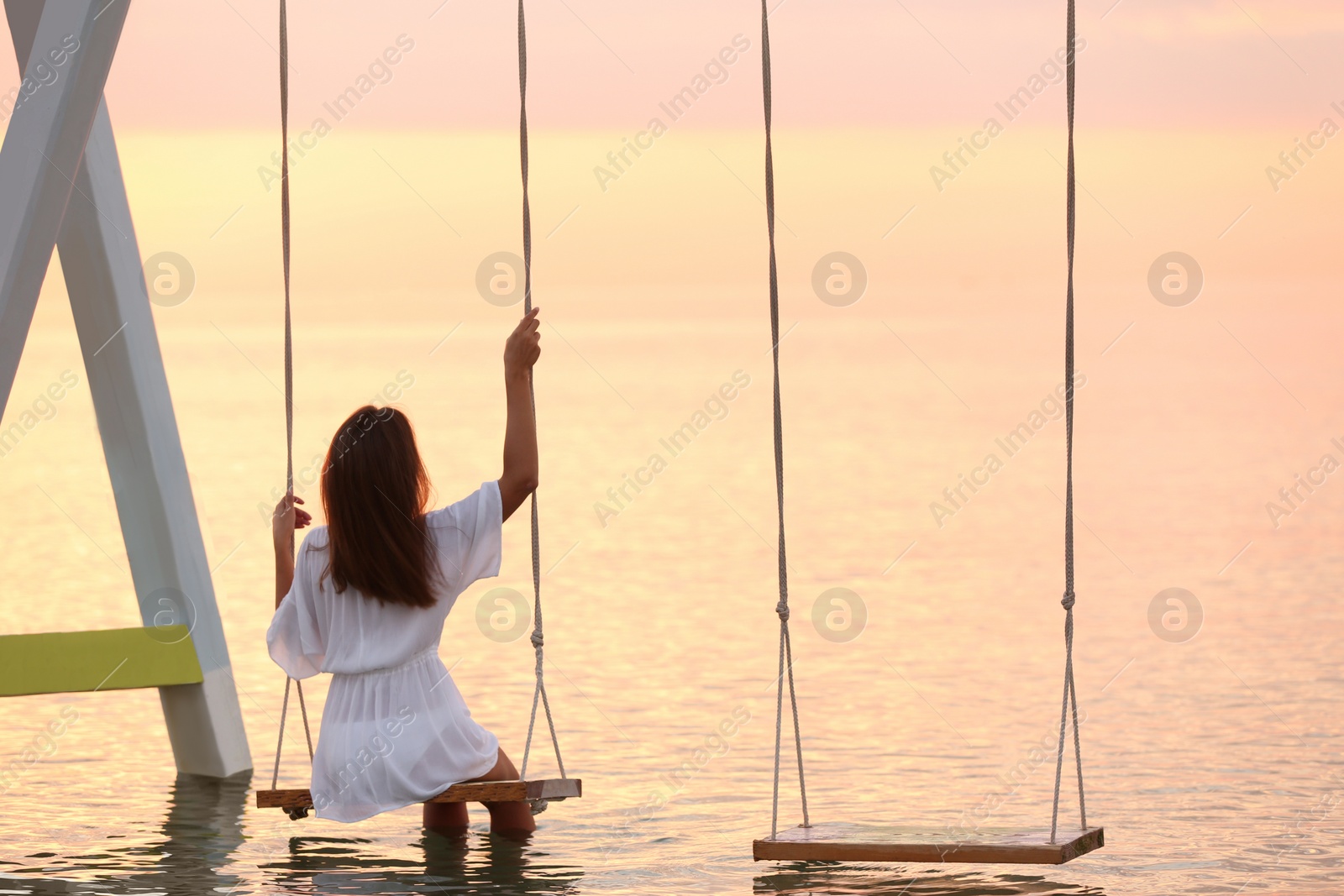 Photo of Young woman enjoying sunrise on swing over water