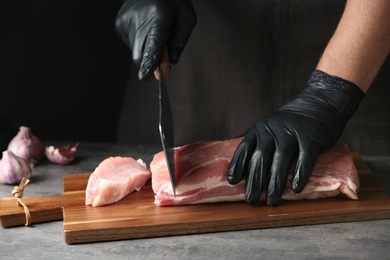 Photo of Man cutting fresh raw meat on table against dark background, closeup