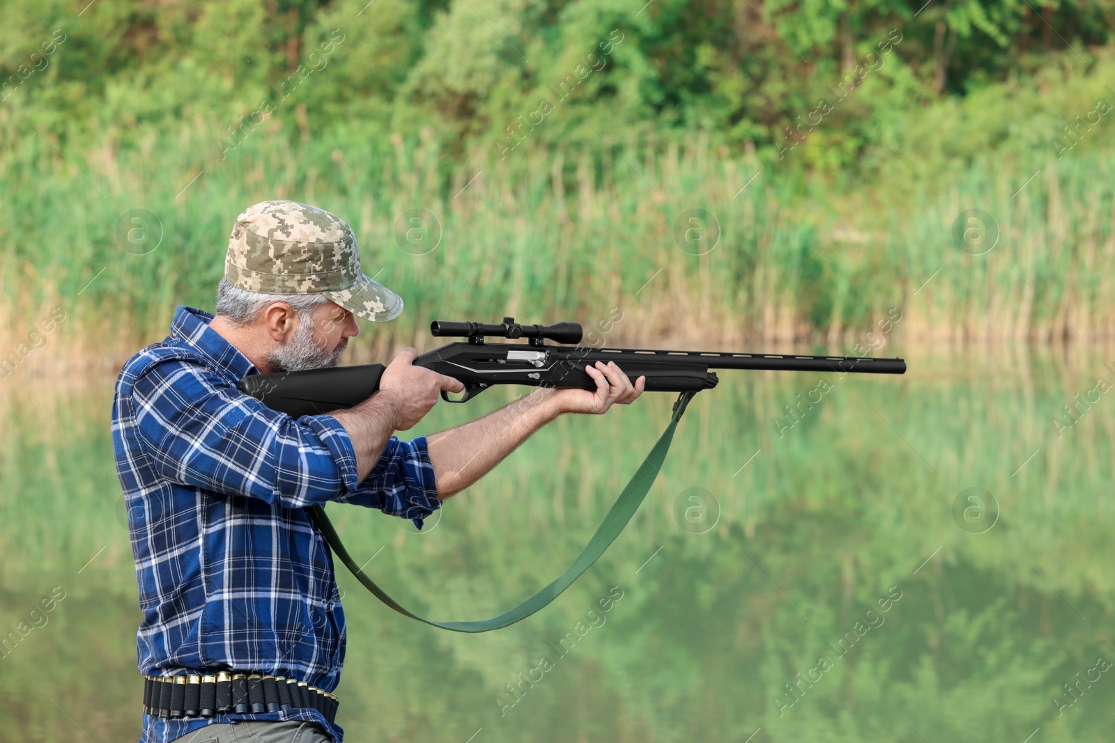 Photo of Man aiming with hunting rifle near lake outdoors