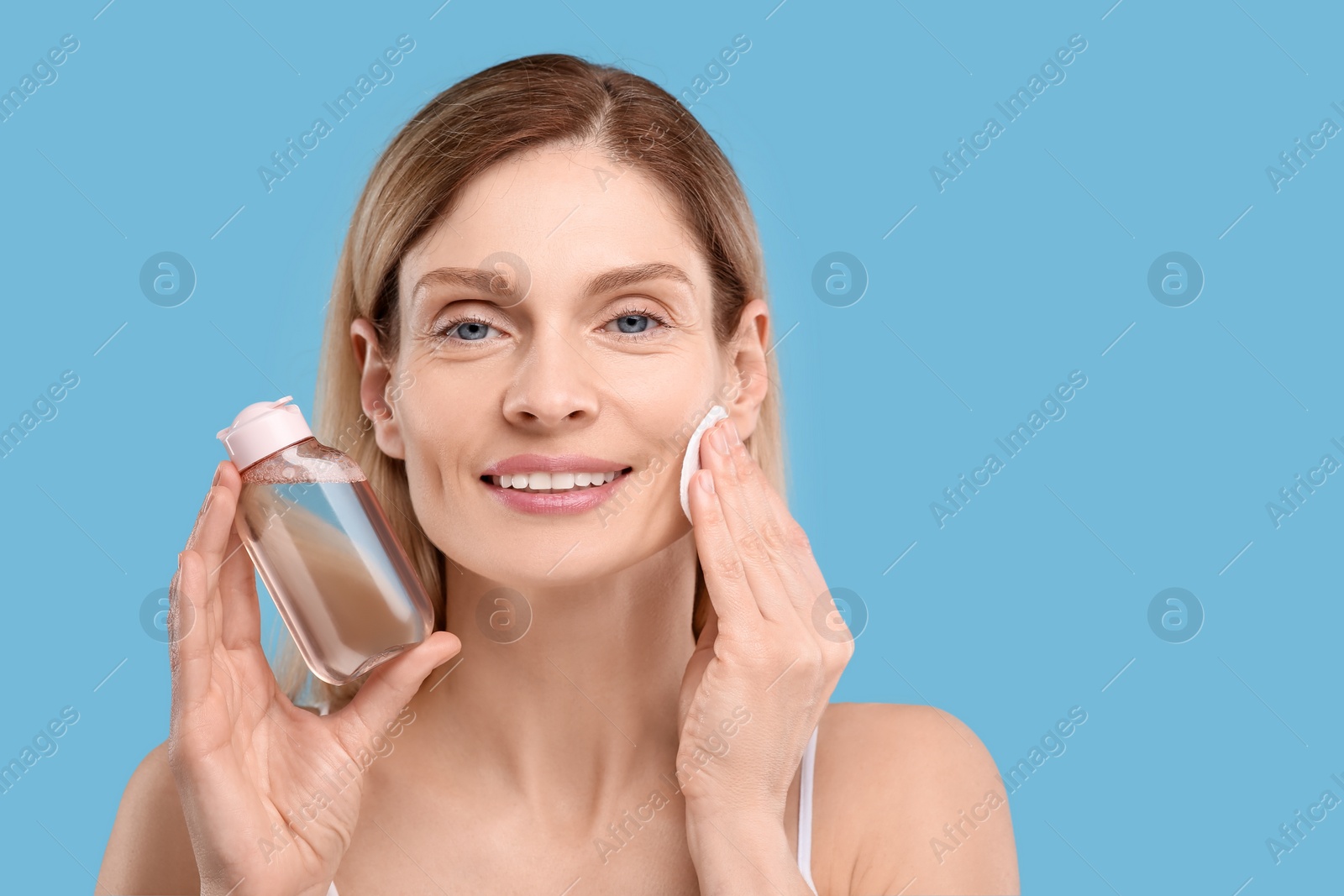 Photo of Beautiful woman removing makeup with cotton pad on light blue background, space for text