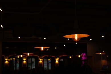 Photo of Lamps with glowing light bulbs in dark restaurant. Space for text