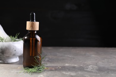 Bottle of essential oil and fresh dill on light gray textured table against black background, space for text