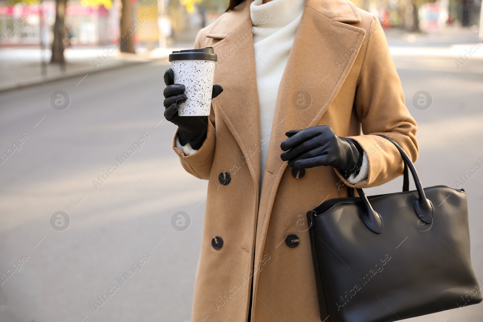 Photo of Woman with stylish leather gloves and cup of coffee on city street, closeup