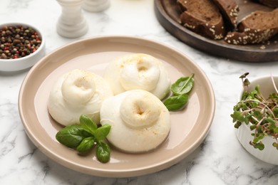Photo of Delicious burrata cheese with basil on white marble table