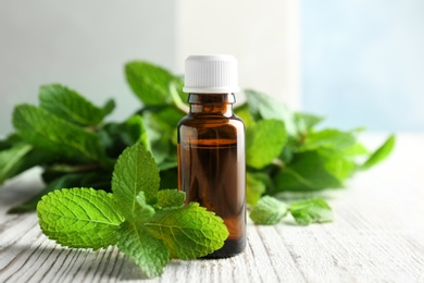 Bottle of essential oil with mint leaves on wooden table