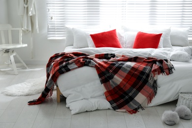 Photo of Comfortable bed with warm checkered plaid in stylish room interior