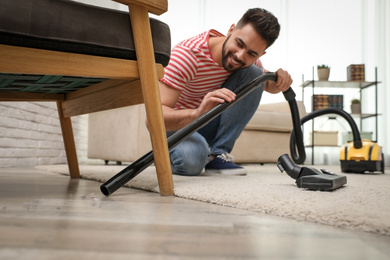 Photo of Young man using vacuum cleaner at home
