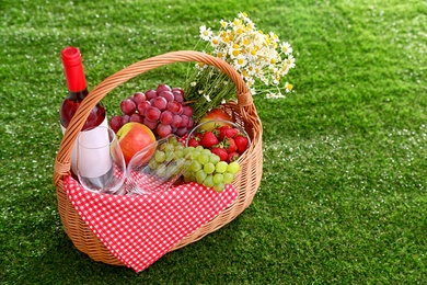 Photo of Picnic basket with wine and products on grass, space for text