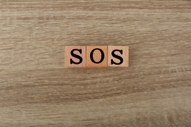 Photo of Abbreviation SOS made of cubes on wooden background, top view