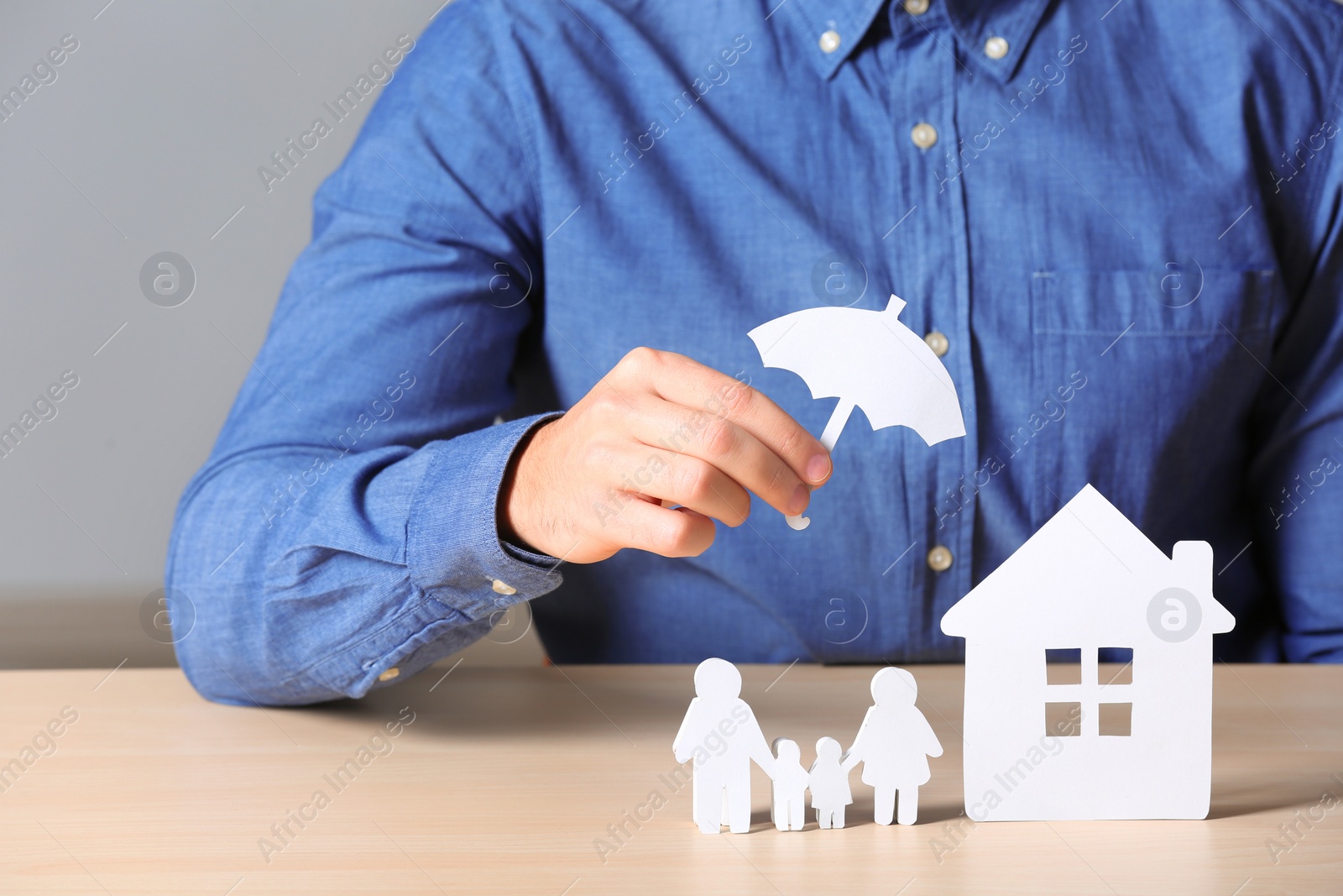 Photo of Male insurance agent covering paper family and home with umbrella cutout at table, closeup