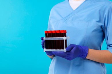 Laboratory testing. Doctor with blood samples in tubes on light blue background, closeup. Space for text