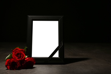 Photo of Empty frame with black ribbon and roses on table. Funeral symbol