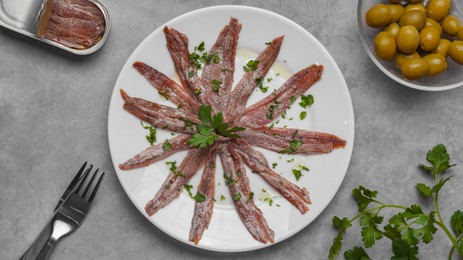 Delicious anchovy fillets, served with olives and parsley on grey table, flat lay