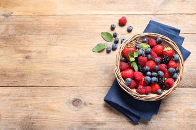 Photo of Wicker basket with many different fresh ripe berries on wooden table, flat lay. Space for text