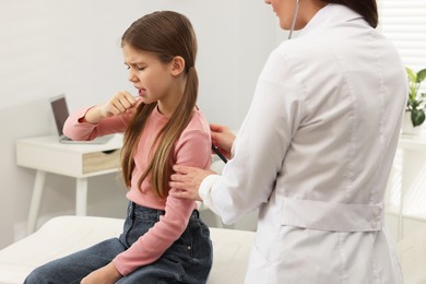 Photo of Doctor examining coughing girl in hospital. Cold symptoms