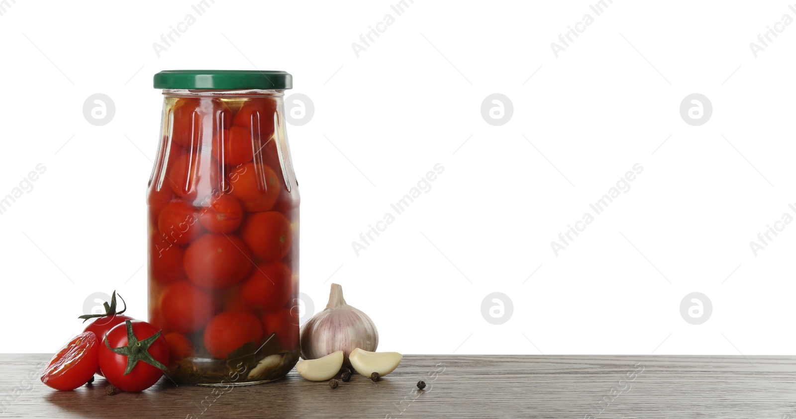 Photo of Glass jar of pickled cherry tomatoes on wooden table against white background. Space for text