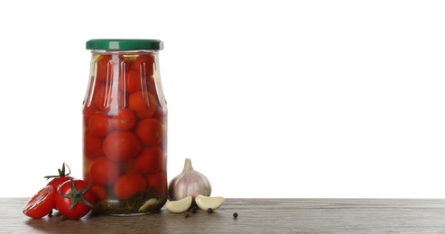 Photo of Glass jar of pickled cherry tomatoes on wooden table against white background. Space for text