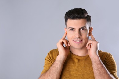 Photo of Man inserting foam ear plugs on grey background. Space for text