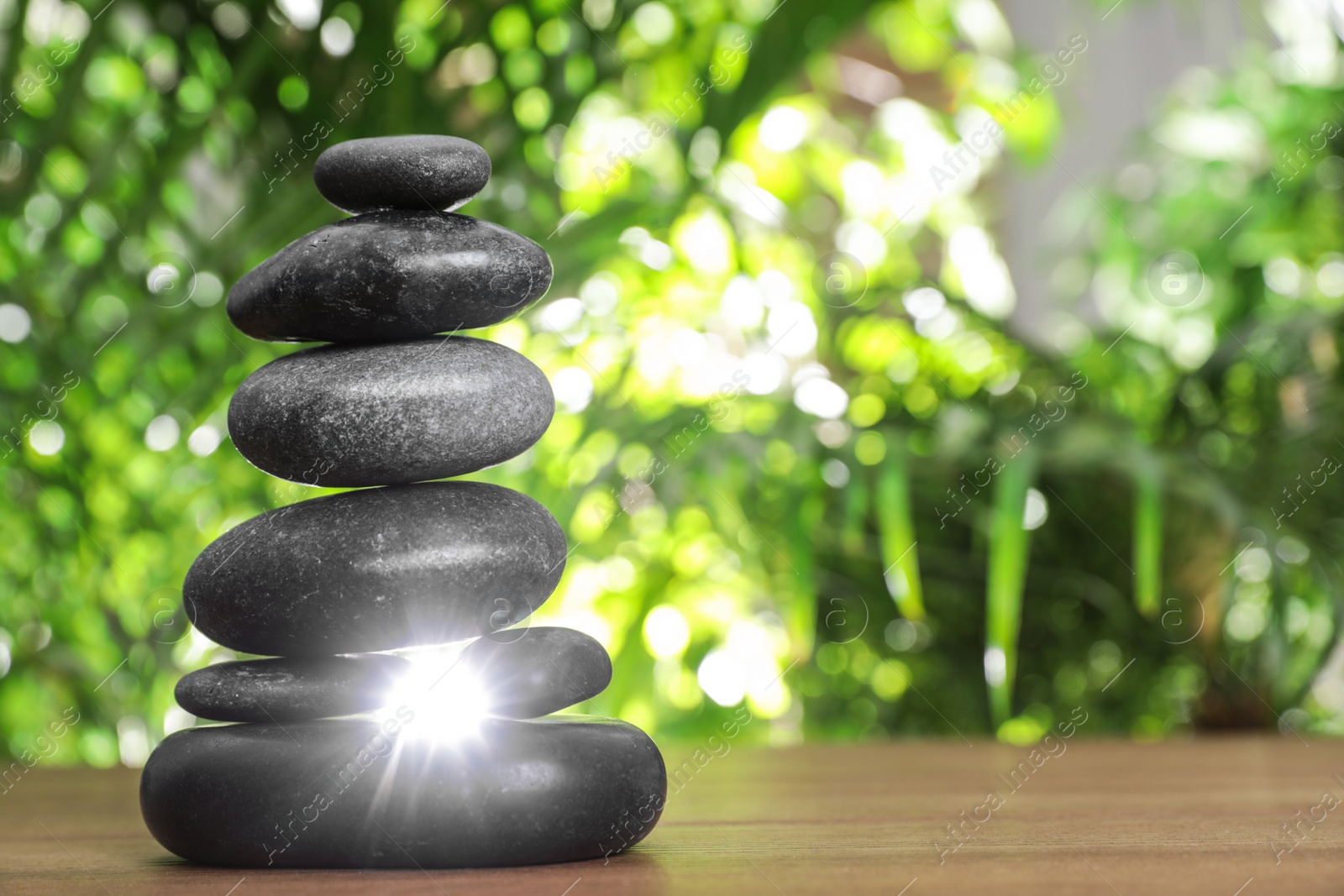 Photo of Table with stack of stones and blurred green leaves on background, space for text. Zen concept