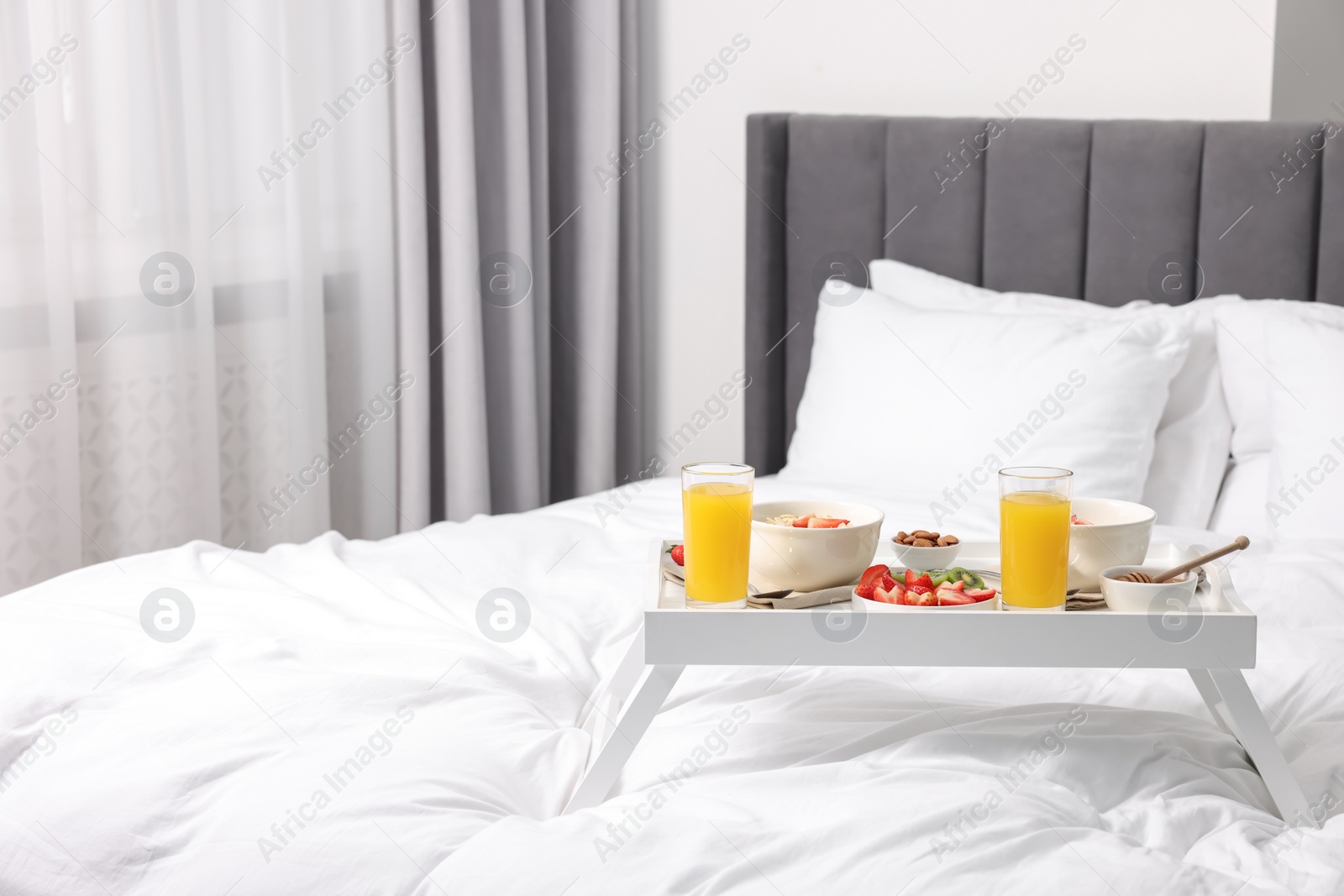 Tasty breakfast served in bed. Oatmeal, juice, fruits, almonds and honey on tray, space for text Photo of Tasty breakfast served in bed. Oatmeal, juice, fruits, almonds and honey on tray, space for text