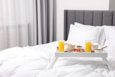 Photo of Tasty breakfast served in bed. Oatmeal, juice, fruits, almonds and honey on tray, space for text