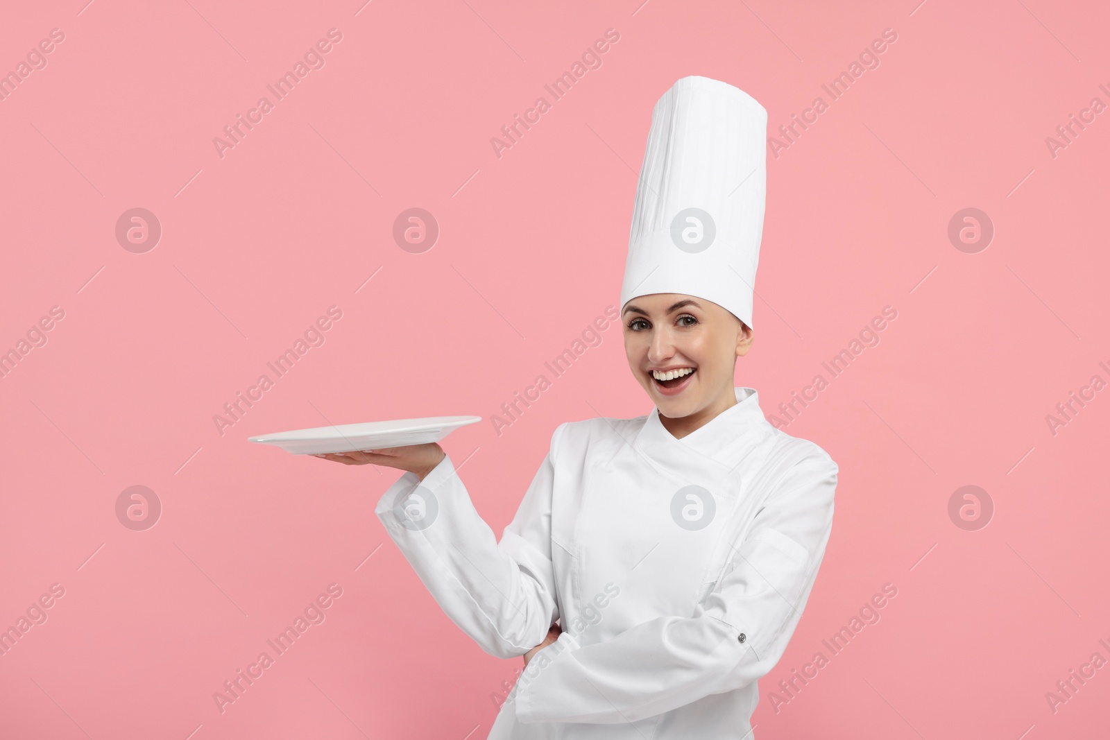 Photo of Happy professional confectioner in uniform holding empty plate on pink background