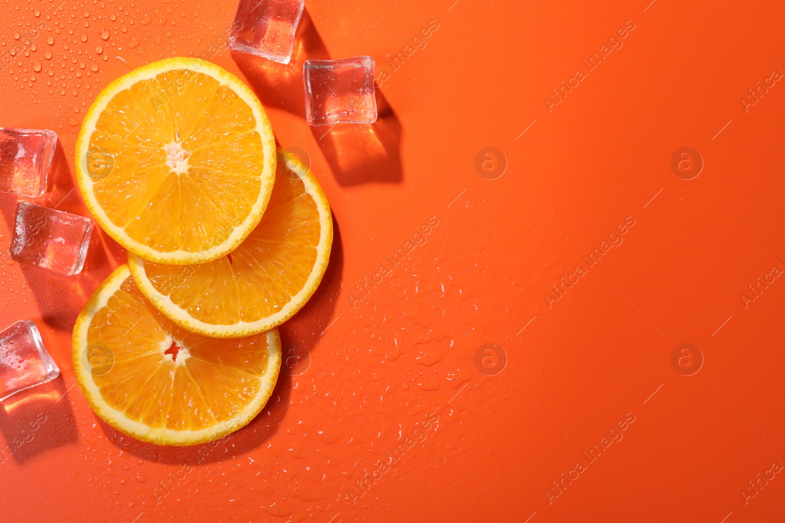 Photo of Slices of juicy orange and ice cubes on terracotta background, flat lay. Space for text
