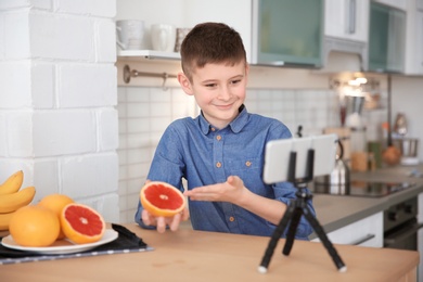 Photo of Cute little blogger with grapefruit recording video on kitchen
