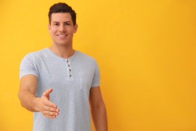 Photo of Man offering handshake against yellow background, focus on hand. Space for text