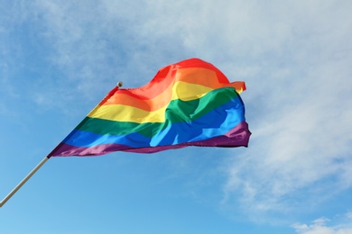 Photo of Bright rainbow gay flag fluttering against blue sky. LGBT community