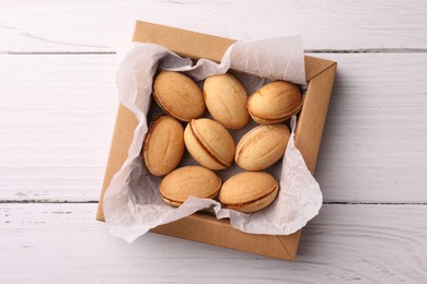 Photo of Delicious nut shaped cookies with boiled condensed milk in box on white wooden table, top view