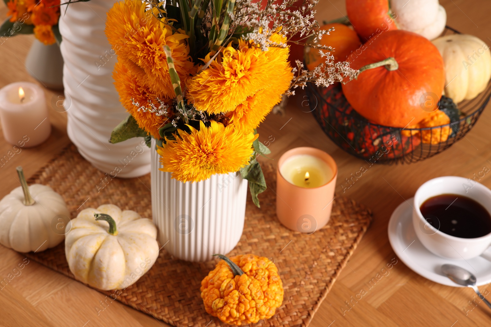 Photo of Autumn atmosphere. Beautiful bright orange flowers, pumpkins, cup of coffee and burning candles on wooden table