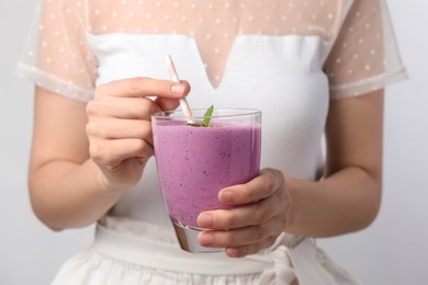 Woman with glass of delicious blackberry smoothie on white background, closeup