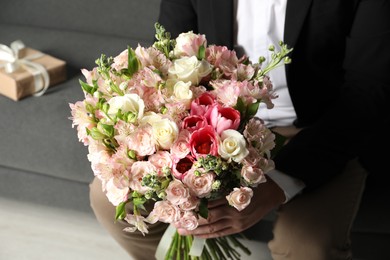 Photo of Man with beautiful bouquet of flowers on sofa indoors, closeup